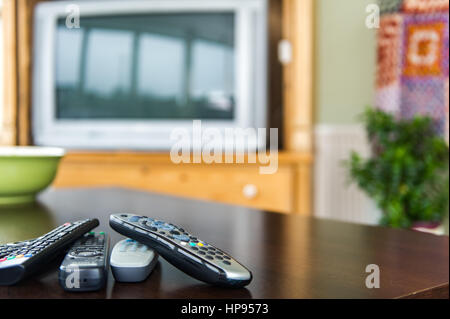 Remote control units on a coffee table in front of a television as a technology concept. Stock Photo