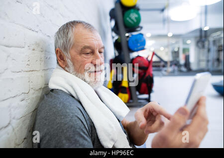 Fit senior man in gym resting, holding smart phone. Stock Photo