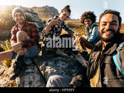 Group of friends resting on mountain while hiking. Hikers relaxing and taking selfie. Stock Photo