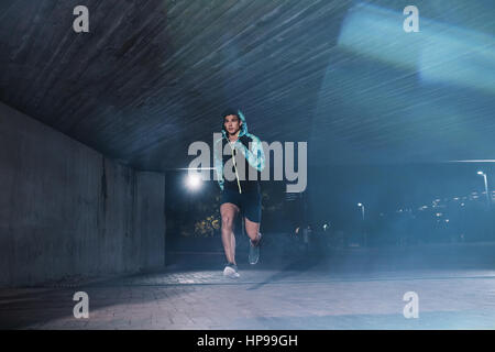 Healthy young man jogging in the city at night. Full length shot of male athlete running under bridge.