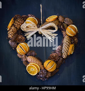 Christmas heart wreath made from pine cones and dried oranges on a plain wooden background Stock Photo