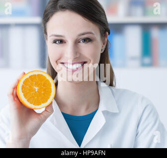 Smiling nutritionist holding a sliced orange, vitamins and healthy diet concept Stock Photo