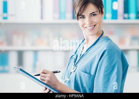 Smiling young female doctor writing a medical report on a clipboard, healthcare professionals Stock Photo