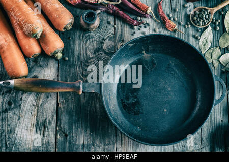 Blank black cast iron pan among the fresh vegetables and spices on gray wooden surface, vintage toning Stock Photo