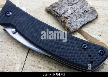 Hunting knife folded on the stump. Black knife with white blade. Stock Photo