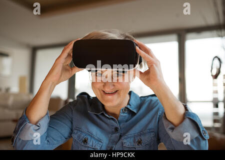 Senior woman wearing virtual reality goggles at home Stock Photo