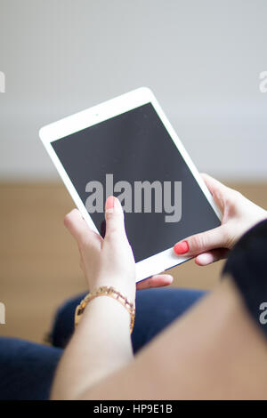 A Caucasian woman with red nails holds a white iPad Stock Photo