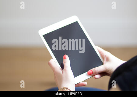 A caucasian woman with red nails holds a white iPad Stock Photo