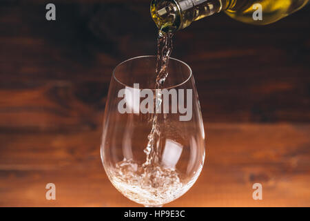 Pouring white wine from a bottle in a close up view of the wineglasses against wooden background Stock Photo