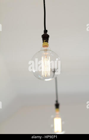 A modern Edison style LED light bulb hangs from a white ceiling Stock Photo