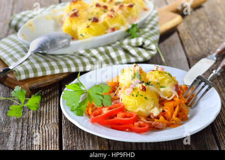 Hearty potato dumplings gratin with cheese and bacon served on paprika cabbage Stock Photo