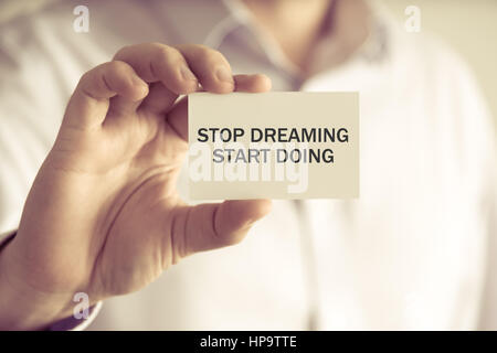 Closeup on businessman holding a card with text STOP DREAMING START DOING, business concept image with soft focus background and vintage tone Stock Photo