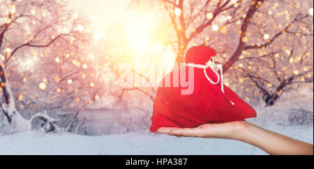 holiday sales background. Red sack in hand on winter background. Red bag with presents on christmas backdrop. Stock Photo