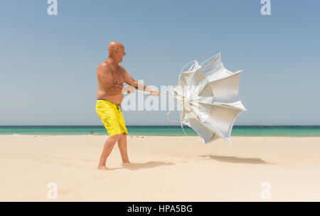 Man with sun umbrella on a windy day. Tarifa, Costa de la Luz, Cadiz, Andalusia, Spain. Stock Photo