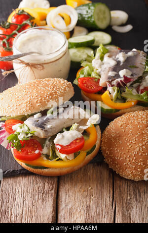 German herring sandwich with sauce and vegetables on a table close-up. vertical Stock Photo