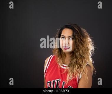 Young Indian woman with long hair, smiling and wearing a sleeveless red sports jersey, black background Stock Photo
