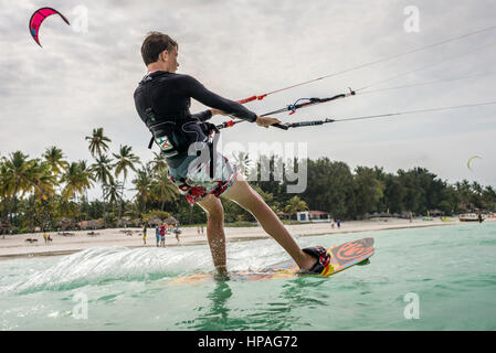 A boy flying kite on a beach of Paje, Zanzibar, Tanzania. Paje is a windy place for good kiting and kitesurfing and at the same time, it is safe for beginners training. This kind of sport gathers thousands of tourists in Paje every season. Stock Photo