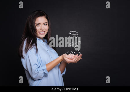 So nice. Pleasant delighted cheerful woman smiling and holding flower while standing on black background Stock Photo