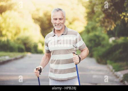 Practicing Nordic walking. Joyful pleasant nice couple using poles and walking while having a morning workout Stock Photo
