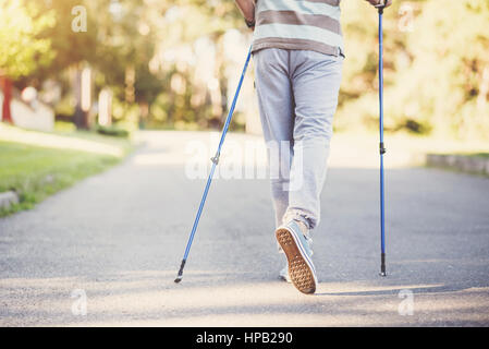 Movement is life. Nice pleasant sporty man holding poles and taking a step while practicing Nordic walking Stock Photo