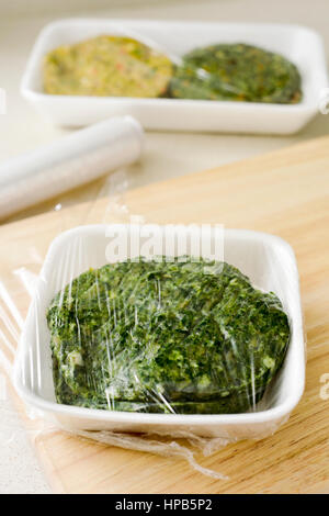 closeup of some different raw veggie burgers in plastic trays covered with plastic wrap ready to be introduced in the fridge or in the freezer Stock Photo