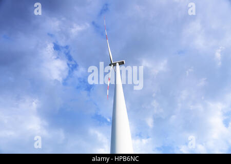 Close up of wind power plant. White power plant on blue sky background. One wind turbine on cloudy sky. Green energy concept. Renewable sources of ene Stock Photo