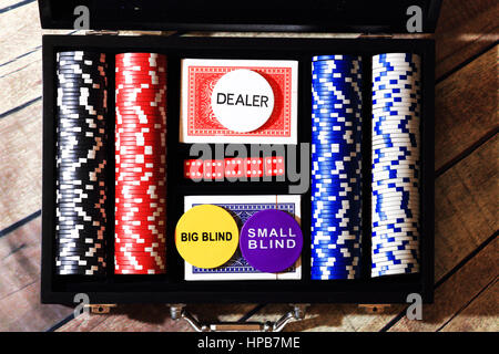 Top view of black suitcase with poker chips cards and dice. Color chips in black suitcase. Dealer big blind and small blind chips on cards on wooden t Stock Photo