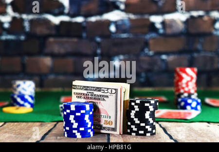 Close up of money between casino chips on poker play background. Dollars on wooden table on brick wall background. Online casino background. Stock Photo