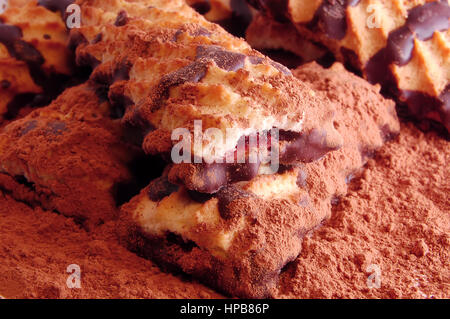 Pile of shortbread cookies with jam and chocolate icing on the scattered cocoa powder close up. Stock Photo