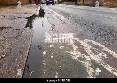 Poor quality broken bicycle / bike / cycle lane / lanes with a cracked / failing surface & pot hole / holes / puddle / puddles. Ashford. Middlesex UK Stock Photo