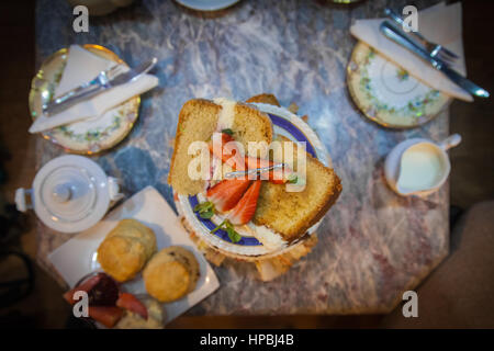 Afternoon High Tea. An overhead image of cake decorated with strawberries, scones, milk, plates and cutlery on a marble table. Stock Photo