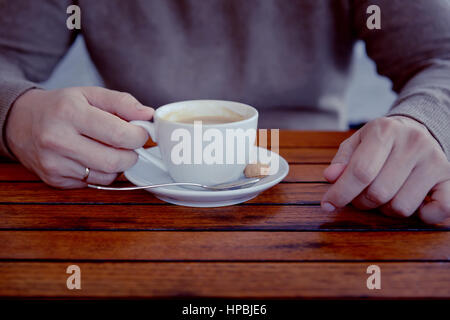 Detail of man's hand holding a spoon stirring a cup of espresso coffee,break time,outdoor Stock Photo