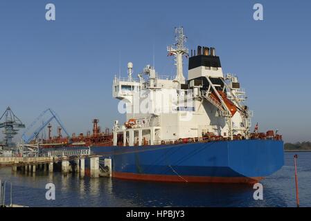 Products Tanker discharging at the Oil Terminal with blue hull and red main deck on sunny day. Stock Photo