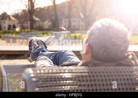Portrait from behind of young male relaxing on a metal bench in a park.Full length of man relaxing  in a city park Stock Photo