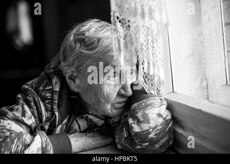 Granny older woman sadly looking out the window. Black-and-white photo. Stock Photo