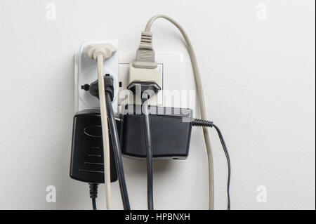 Multiple electrical plugs in wall outlet, dangerous concept Stock Photo