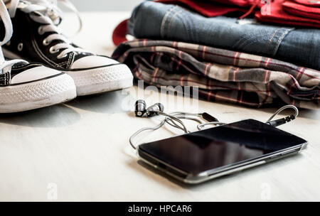 Clothes & accessories: hipster sneakers, denim, plaid shirt, cowboy belt, phone with headphones on wooden background. Traveling concept Stock Photo