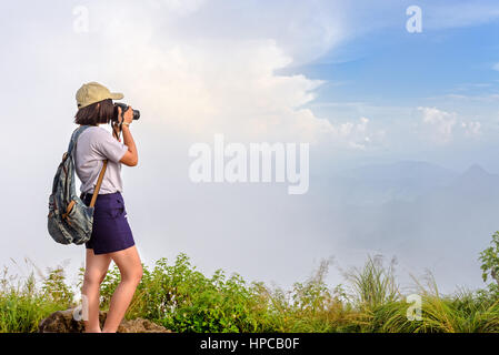 Hiker asian teens girl with digital camera and backpack taking photo beautiful natural of sierra sky cloud and fog during sunset in winter on mountain Stock Photo