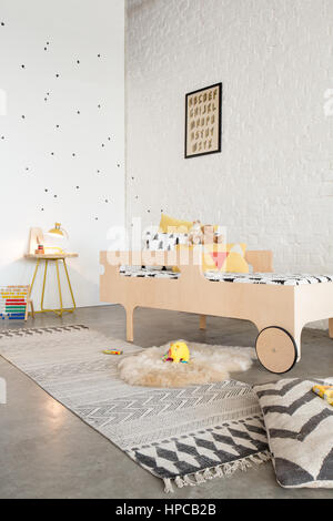 A bed in a child's bedroom with white walls and poured concrete floor