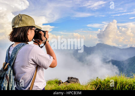 Hiker asian teens girl with digital camera and backpack taking photo beautiful natural of sierra sky clouds and fog during sunset in winter on mountai Stock Photo