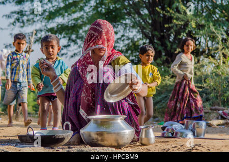 RAJASTHAN, INDIA - NOVEMBER 20, 2016: Rajasthani poor woman cleaning utensils after cooking meal for her family, four children playing in the backgrou Stock Photo