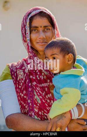 RAJASTHAN, INDIA - NOVEMBER 20, 2016: Unidentified Rajasthani poor woman wearing traditional costume and red sari holding her young son. Stock Photo