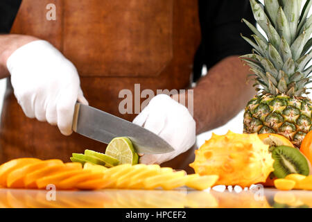 Chef slicing lime on a wooden cutting board among other tropical fruits Stock Photo