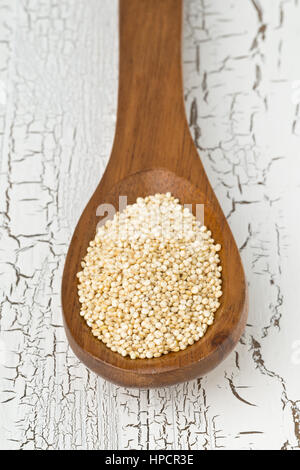 Raw unprocessed quinoa seeds in wooden spoon on white rustic wooden table Stock Photo
