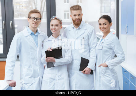 Team of young professional scientists in white coats smiling at camera in laboratory Stock Photo