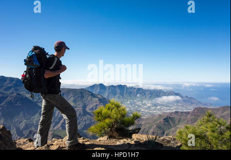 Mature male hiker on Alta Vista mountain on Gran Canaria with La Aldea de San Nicolas village in distance. Canary Islands. Spain Stock Photo