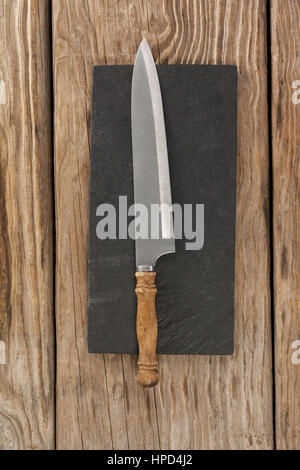 Knife on black slate plate against wooden background Stock Photo