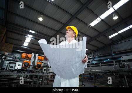 Thoughtful factory engineer holding blueprint in bottle factory Stock Photo