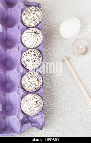 Decorating Easter eggs using a traditional wax-resist method and modern patterns. Eggs in a purple paper box with molten wax applied to the white shel Stock Photo