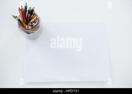 Colored pencils kept in pencils holder kept on blank paper on white background Stock Photo